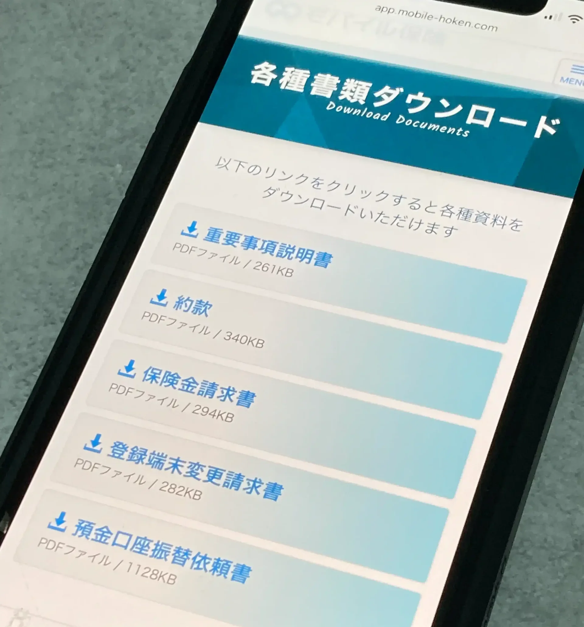 モバイル保険のマイページの各種書類ダウンロード画面（重要事項説明書・約款・保険金請求書・登録端末変更請求書・預金口座振替依頼書）をスマホで撮影した写真